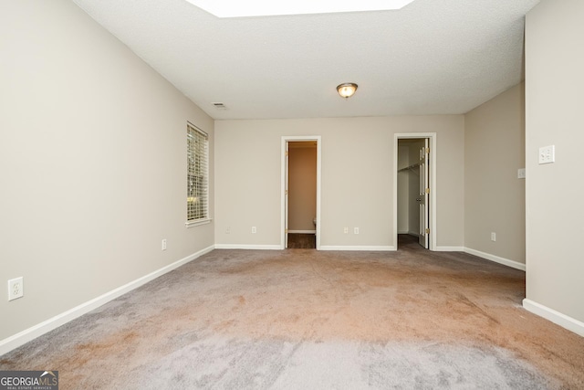 unfurnished bedroom with carpet floors, a walk in closet, a closet, and a textured ceiling