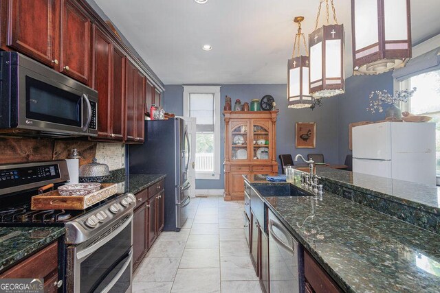 kitchen with backsplash, sink, hanging light fixtures, dark stone countertops, and appliances with stainless steel finishes