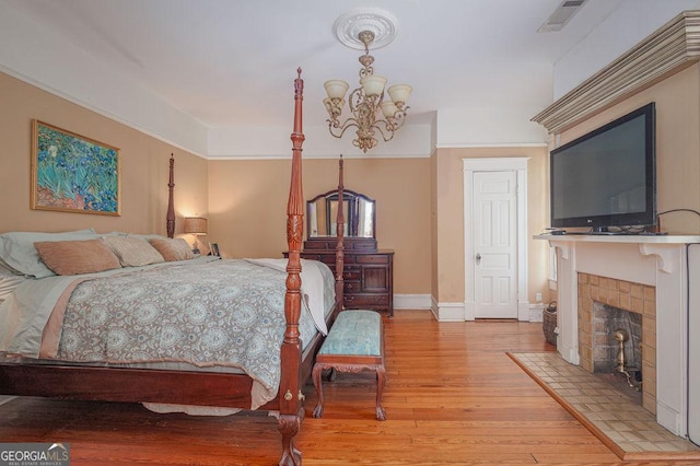 bedroom featuring light hardwood / wood-style floors, an inviting chandelier, and a tiled fireplace