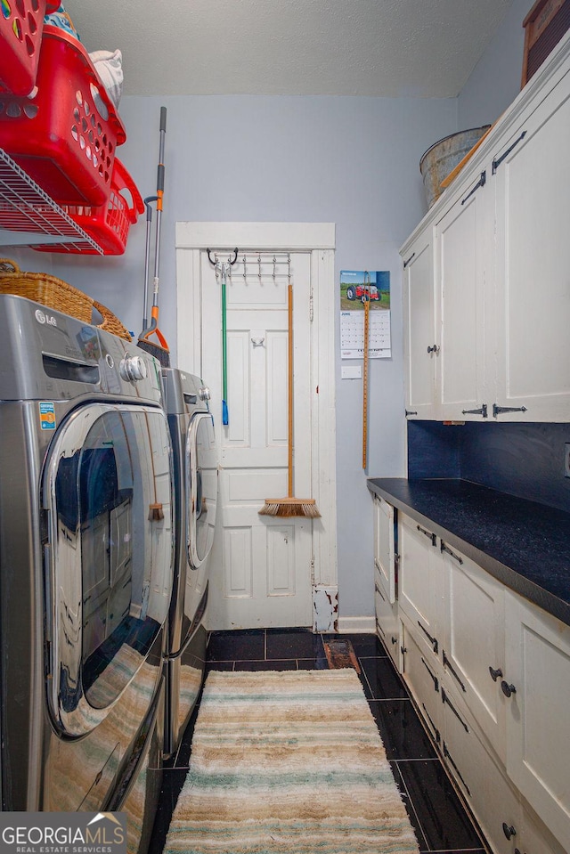 clothes washing area featuring washer and clothes dryer, dark tile patterned floors, and cabinets