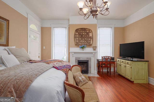 bedroom with an inviting chandelier, wood-type flooring, and a tiled fireplace