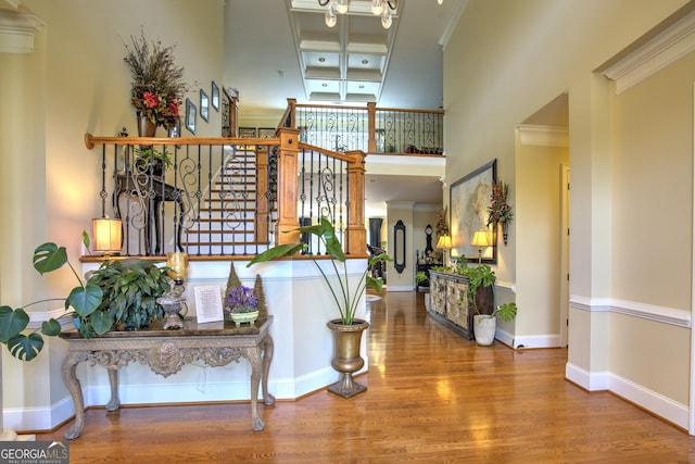 foyer featuring a towering ceiling, wood-type flooring, coffered ceiling, beam ceiling, and ornamental molding