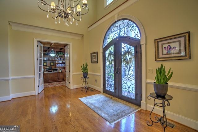 foyer entrance with french doors, hardwood / wood-style floors, and an inviting chandelier