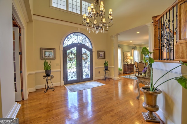 foyer featuring light hardwood / wood-style floors, decorative columns, a chandelier, french doors, and ornamental molding