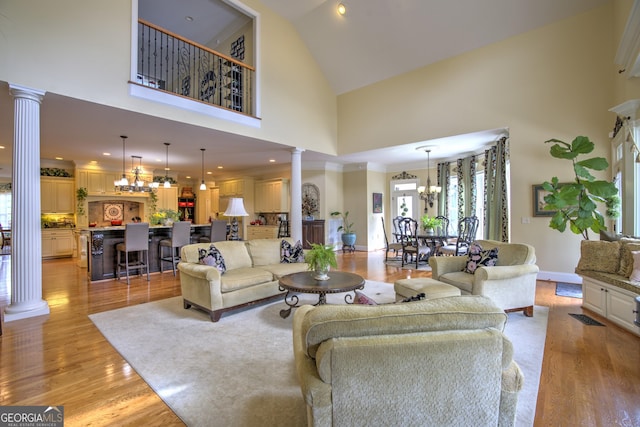 living room featuring a chandelier, a high ceiling, ornate columns, and light hardwood / wood-style floors