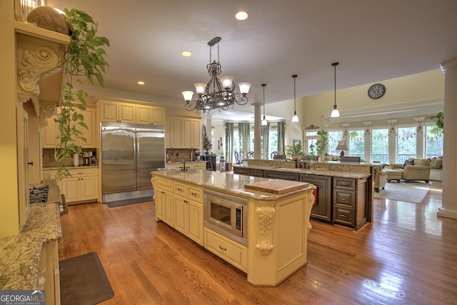 kitchen featuring decorative light fixtures, backsplash, built in appliances, and an island with sink