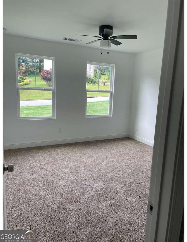 carpeted empty room with ceiling fan and a wealth of natural light