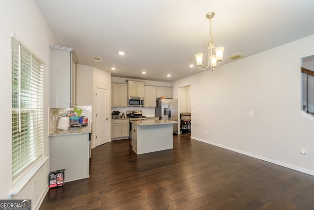 kitchen featuring light stone countertops, appliances with stainless steel finishes, a kitchen island, decorative light fixtures, and an inviting chandelier