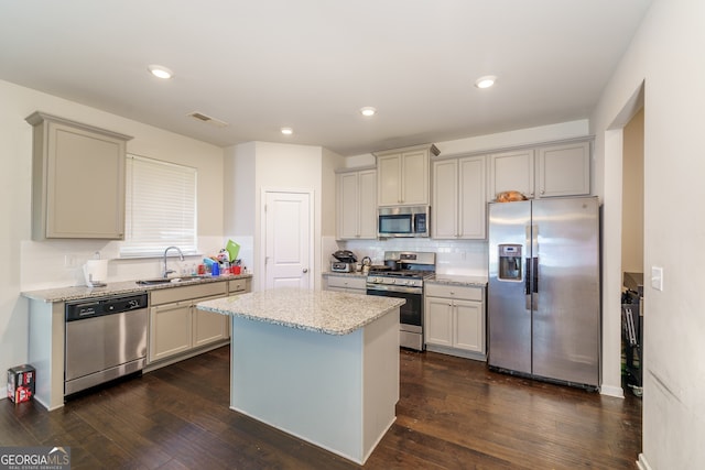 kitchen with appliances with stainless steel finishes, sink, dark wood-type flooring, tasteful backsplash, and a center island