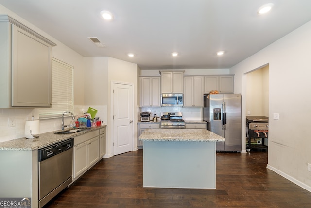 kitchen featuring a center island, appliances with stainless steel finishes, sink, dark wood-type flooring, and light stone counters