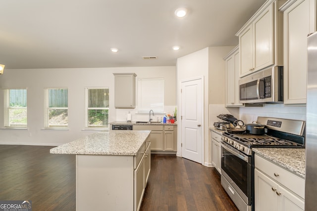 kitchen with appliances with stainless steel finishes, dark wood-type flooring, white cabinetry, light stone countertops, and a center island