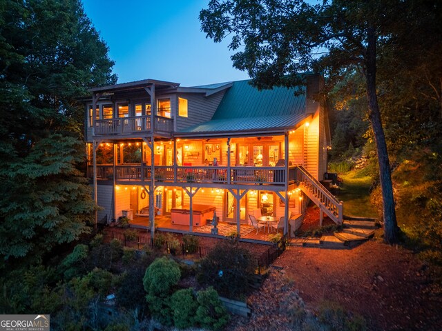 rear view of house featuring a balcony, a patio, a chimney, metal roof, and a hot tub