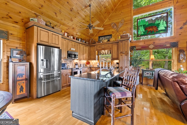 kitchen featuring high vaulted ceiling, stainless steel appliances, wood walls, and a kitchen breakfast bar