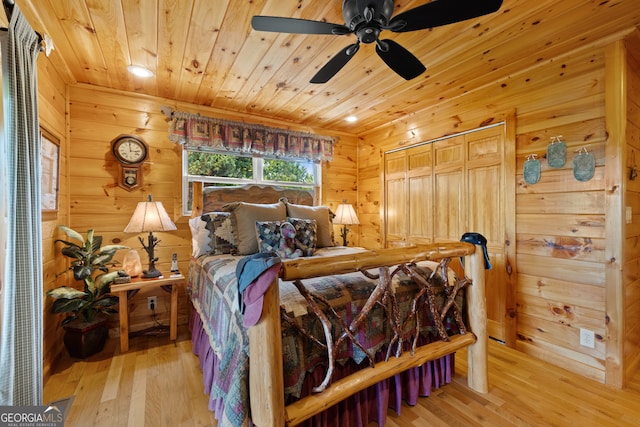 bedroom with a closet, wooden walls, light hardwood / wood-style flooring, wooden ceiling, and ceiling fan