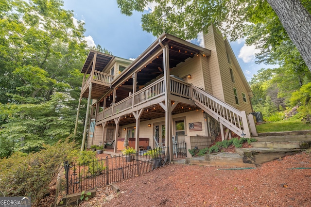 rear view of property featuring a deck, a chimney, a patio area, a hot tub, and stairway