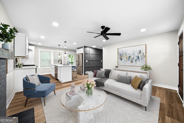 living room featuring sink, a fireplace, ceiling fan, and light wood-type flooring