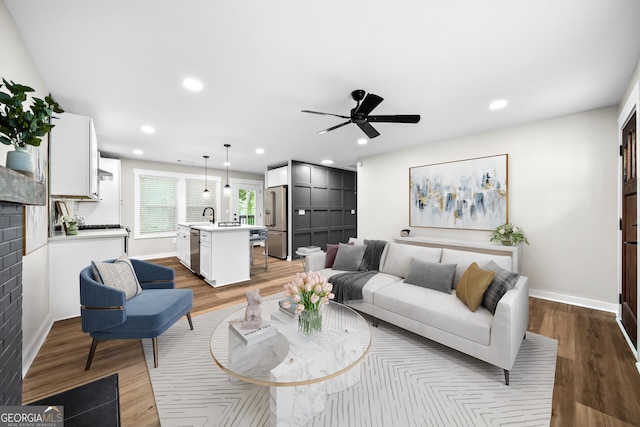 living room with ceiling fan, sink, and light wood-type flooring