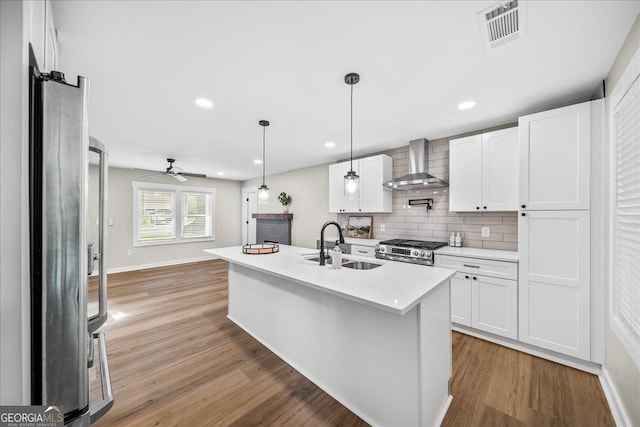 kitchen featuring white cabinetry, wall chimney range hood, sink, and appliances with stainless steel finishes