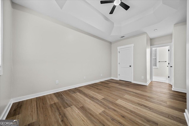 unfurnished bedroom with hardwood / wood-style floors, ceiling fan, and a tray ceiling