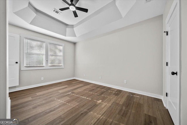 empty room featuring ceiling fan, wood-type flooring, and a tray ceiling