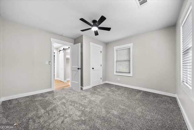 unfurnished bedroom with a barn door, carpet floors, and ceiling fan