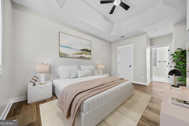 bedroom with ceiling fan, a tray ceiling, and light wood-type flooring