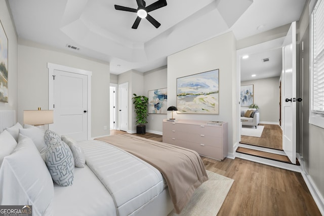 bedroom with ceiling fan, a tray ceiling, and light hardwood / wood-style flooring