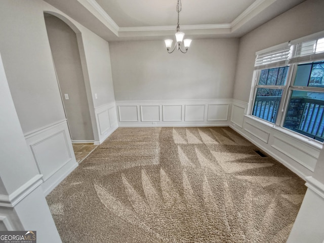 empty room featuring a raised ceiling, a notable chandelier, light colored carpet, and crown molding