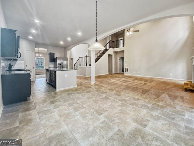 kitchen with sink, ceiling fan, stainless steel fridge, an island with sink, and decorative light fixtures