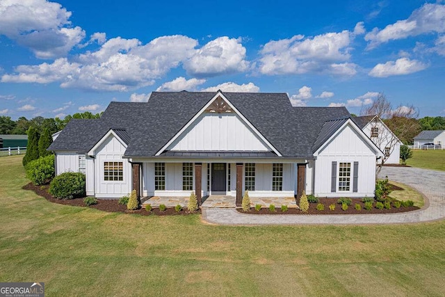 modern inspired farmhouse featuring covered porch, a shingled roof, board and batten siding, and a front yard