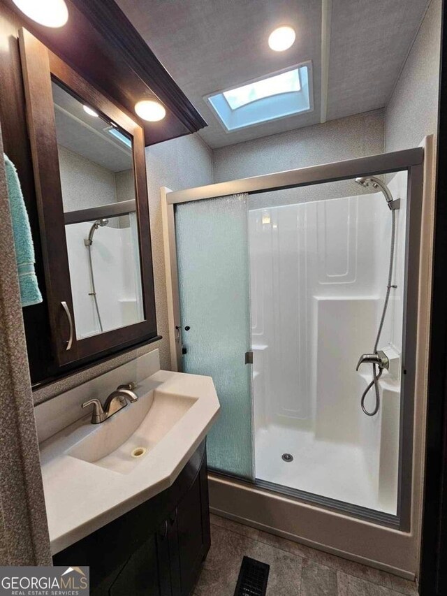 bathroom with a skylight, a shower with shower door, vanity, and tile patterned floors