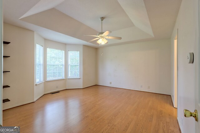 unfurnished room featuring ceiling fan, a tray ceiling, and light wood-type flooring