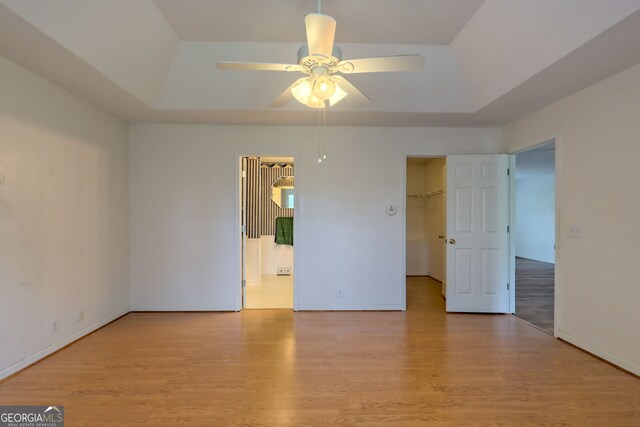 empty room with light hardwood / wood-style flooring, a raised ceiling, and ceiling fan