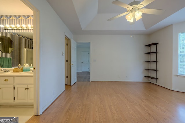 empty room featuring sink, ceiling fan, a raised ceiling, and light hardwood / wood-style flooring