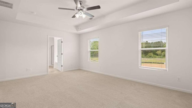 empty room with a tray ceiling, ceiling fan, light colored carpet, and a healthy amount of sunlight