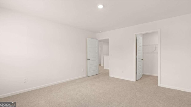 unfurnished bedroom with light colored carpet, a walk in closet, and a closet