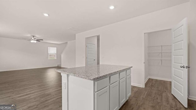 kitchen featuring white cabinets, ceiling fan, light stone countertops, a kitchen island, and dark hardwood / wood-style flooring