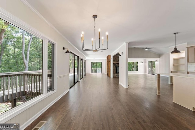 unfurnished dining area featuring a healthy amount of sunlight, dark wood-type flooring, crown molding, and ceiling fan with notable chandelier