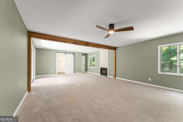 carpeted spare room with a barn door, beam ceiling, a large fireplace, and ceiling fan