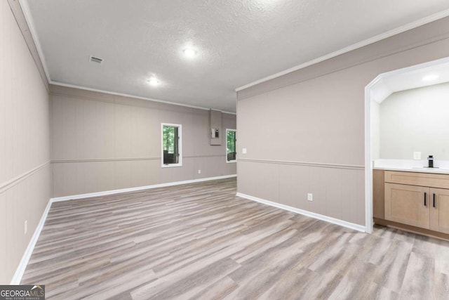 empty room with sink, a textured ceiling, ornamental molding, and light wood-type flooring