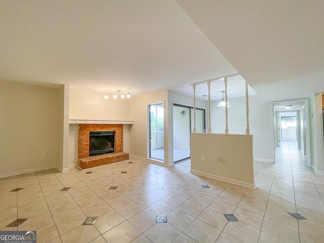 unfurnished living room featuring rail lighting, a wealth of natural light, light tile patterned floors, and a brick fireplace