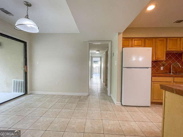 kitchen with decorative backsplash, sink, light tile patterned floors, white refrigerator, and decorative light fixtures