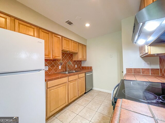 kitchen with tile countertops, white refrigerator, stainless steel dishwasher, and range hood