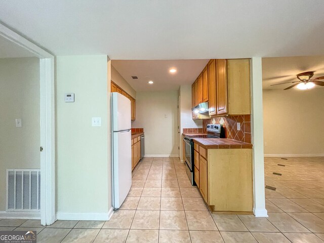 kitchen with tile counters, tasteful backsplash, black electric range, white fridge, and light tile patterned floors