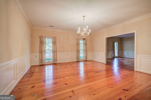 spare room with an inviting chandelier, ornamental molding, and light hardwood / wood-style floors