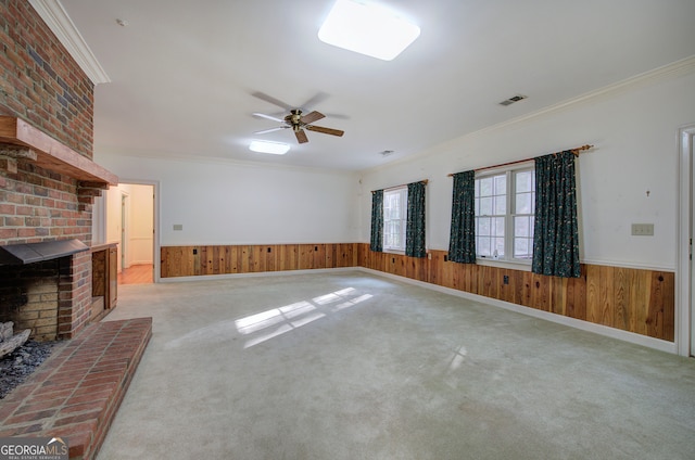 unfurnished living room with light carpet, wood walls, ornamental molding, and a fireplace