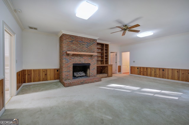 unfurnished living room with wooden walls, ornamental molding, a brick fireplace, and light colored carpet