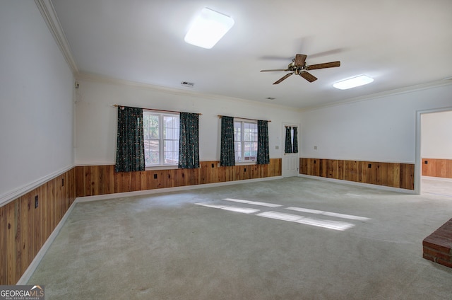 empty room featuring ornamental molding, ceiling fan, carpet flooring, and wood walls