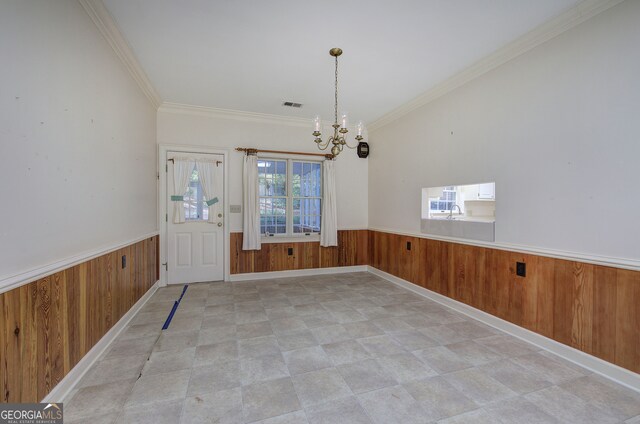 unfurnished dining area featuring wood walls, ornamental molding, and an inviting chandelier