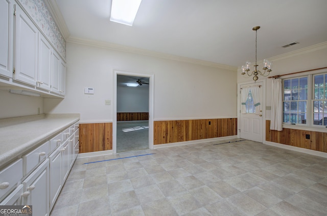 unfurnished dining area with crown molding, ceiling fan with notable chandelier, and wood walls